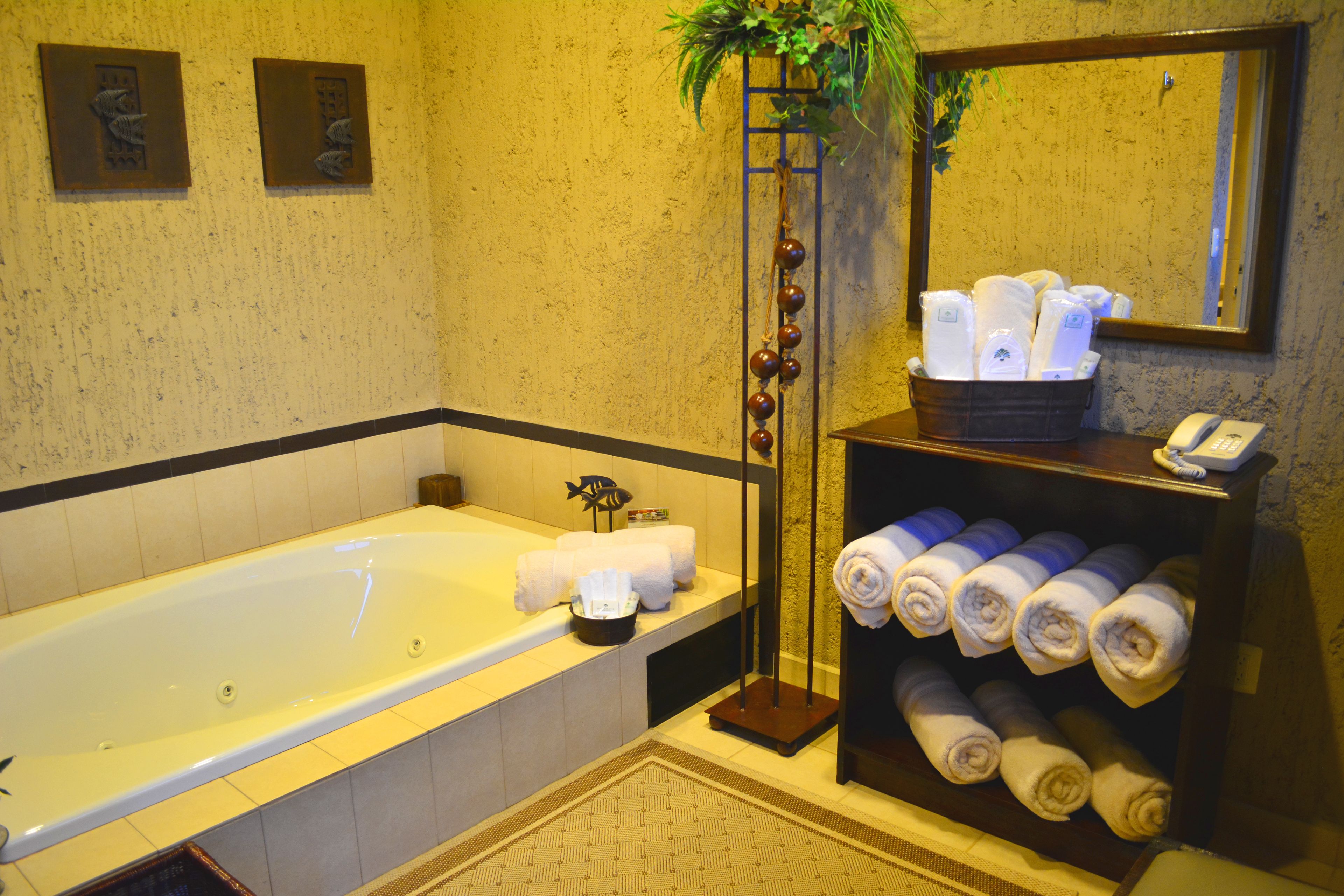 A bathroom with a bathtub, a towel rack with towels, a mirror, and a plant.