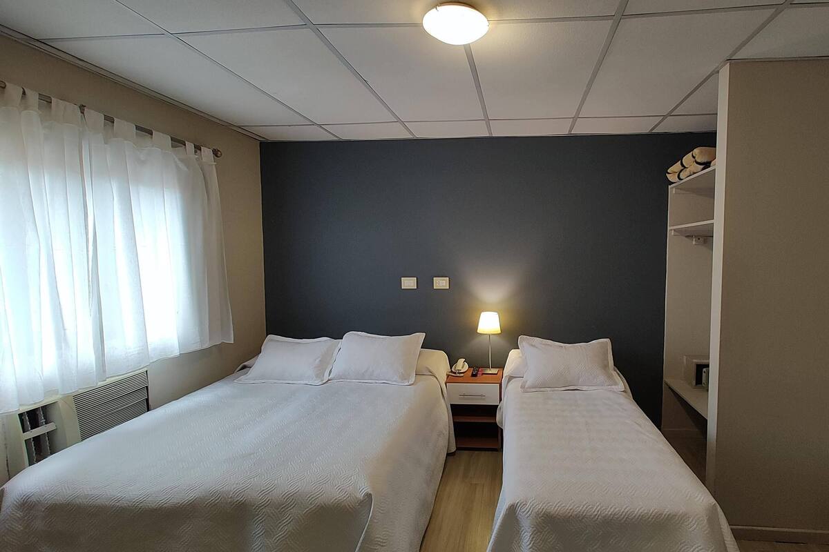 A hotel room with two single beds, a nightstand with a lamp, a small table, and a wardrobe.