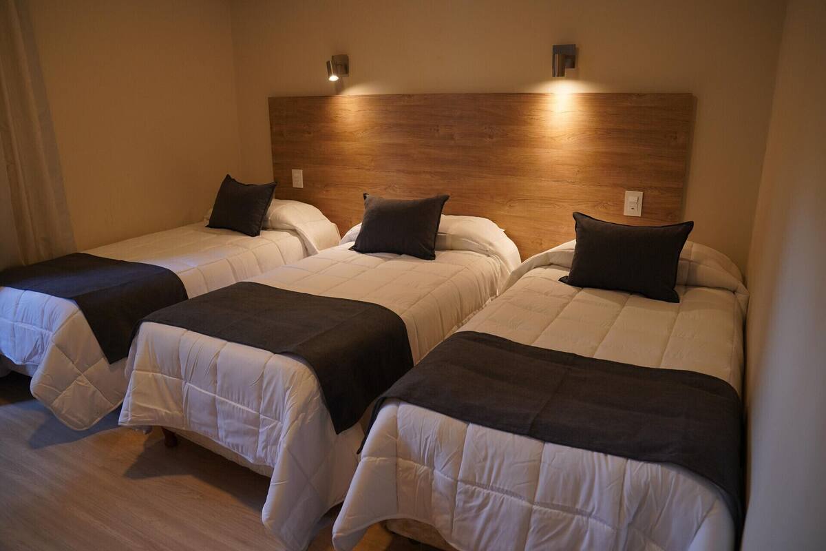 A hotel room with three beds, each with a white duvet and a dark-colored throw.