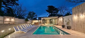 A modern outdoor swimming pool with lounge chairs, a bar area, and a glass-enclosed space. - Alpre Hotel (Villa Carlos Paz)