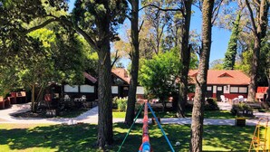 A park with a long, colorful seesaw, trees, and a building with outdoor seating.