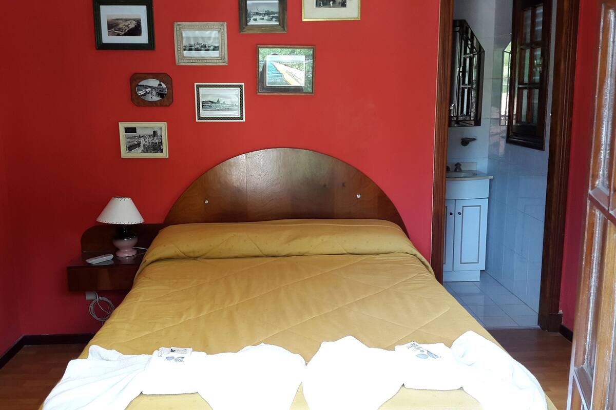 Een kamer met een bed, een nachtkastje met een lamp en een muur met ingelijste foto's.