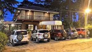 A hotel with a two-story structure, a covered entrance, and a parking area with several SUVs.