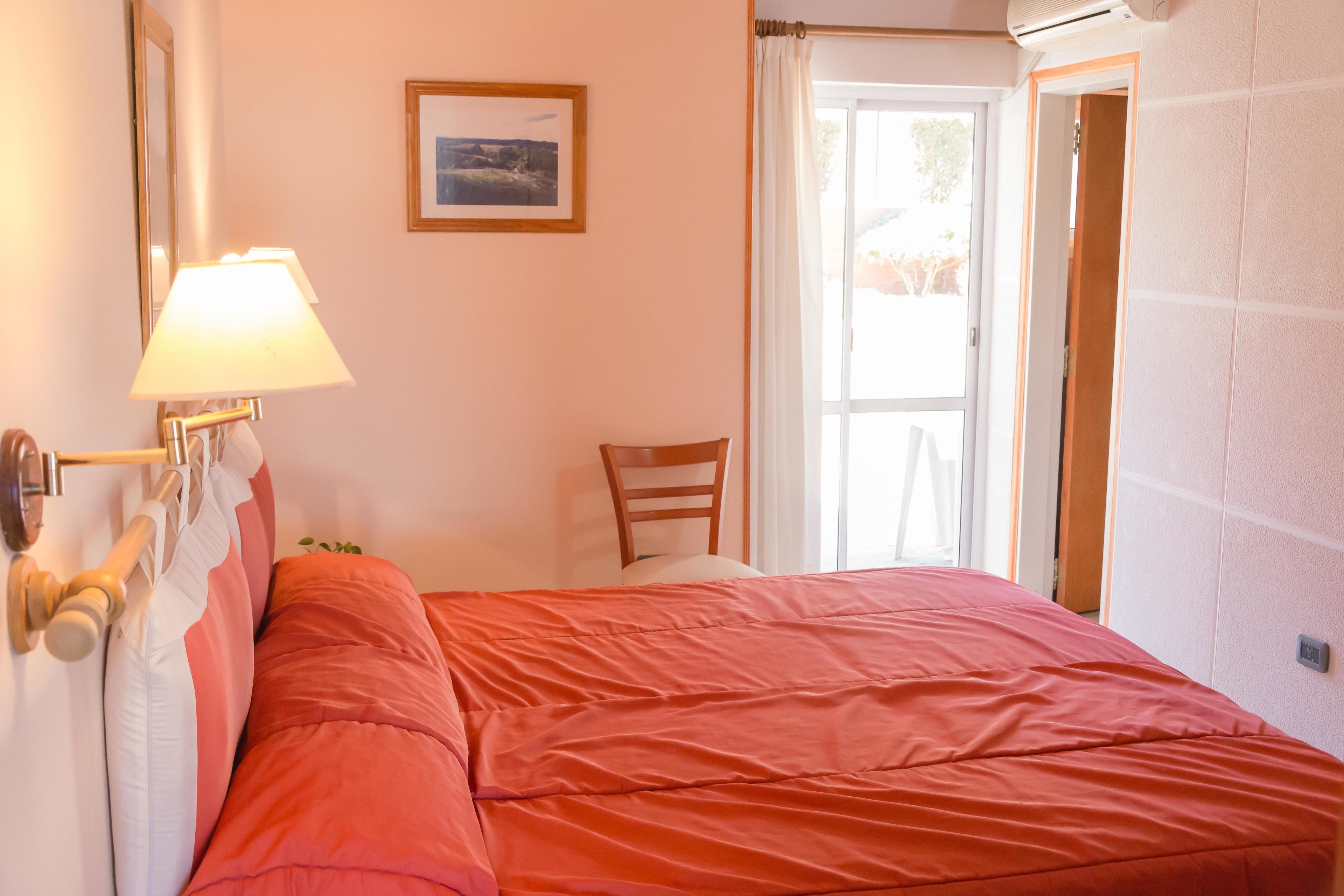 Un dormitorio con cama, una silla, una lámpara, un cuadro en la pared y una puerta que da a un balcón.