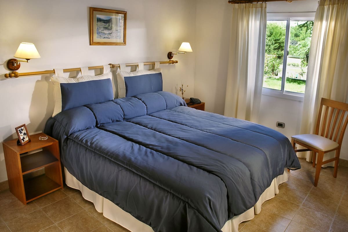 A bedroom with a large bed, two bedside tables, a nightstand, a chair, and a window with curtains.