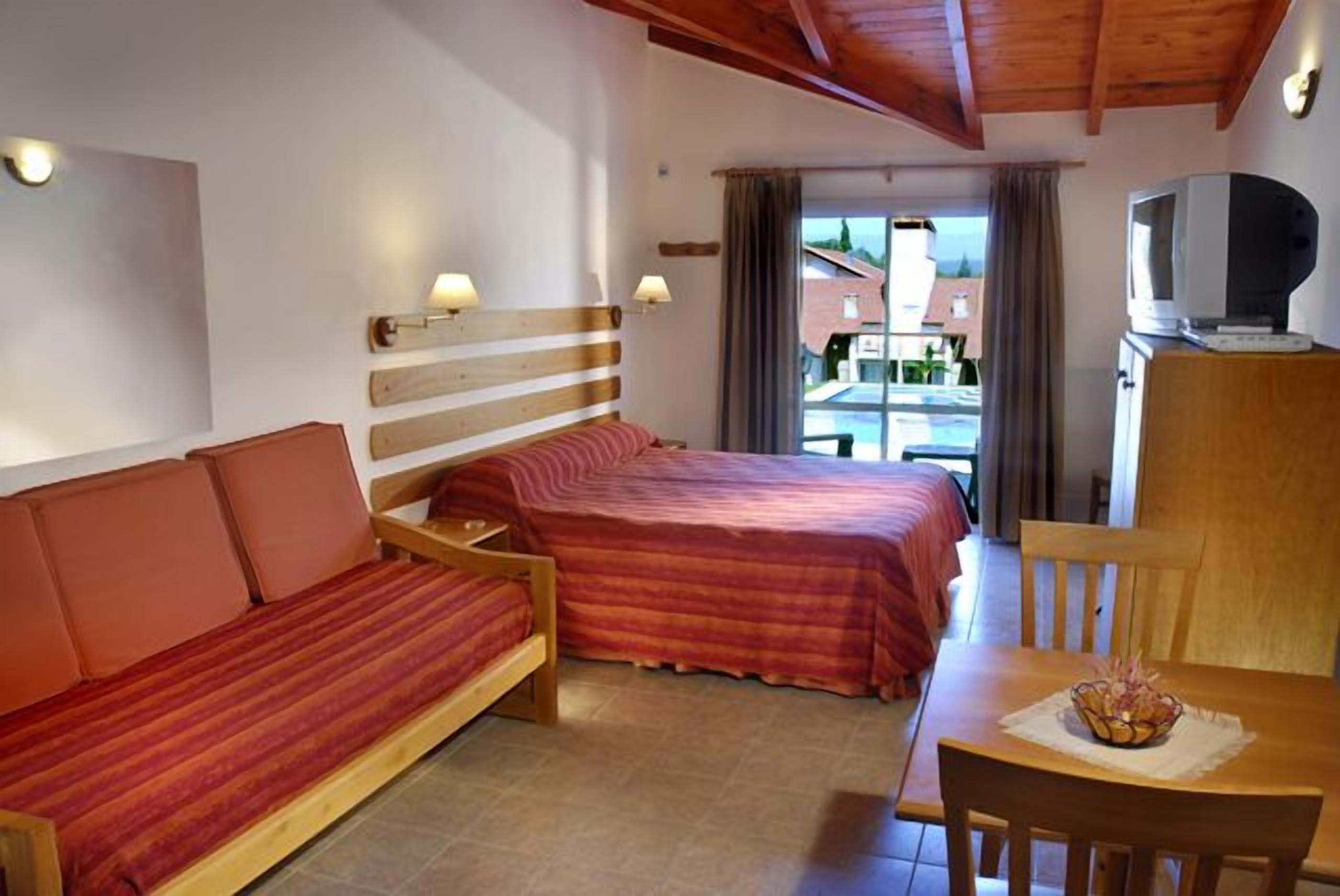 A room with a bed, a sofa, a table with a basket, and a television on a cabinet.