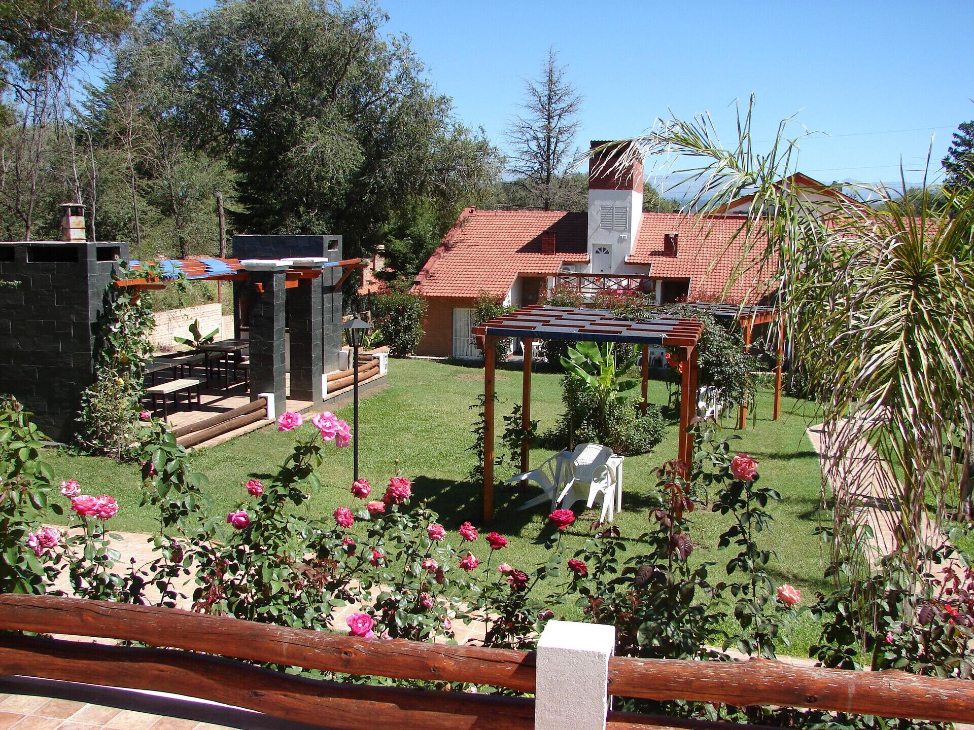 A garden with a pergola, a barbecue area, and a house with a red roof.