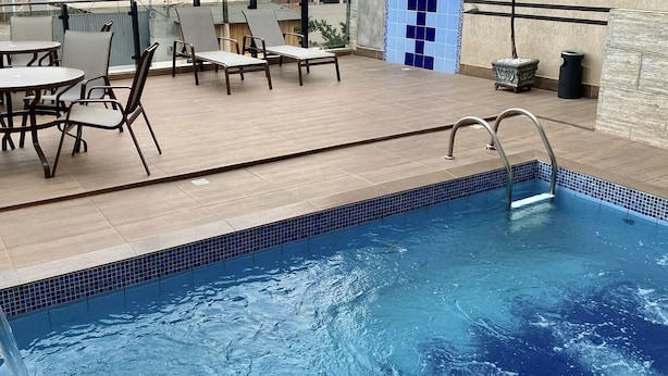 An indoor swimming pool with a tiled edge, surrounded by lounge chairs and a small table. - Hotel Caribe (Porto Velho)
