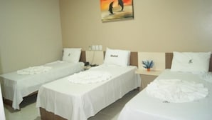 A hotel room with two single beds, a nightstand with a lamp, and a painting on the wall. - Hotel Caribe (Porto Velho)