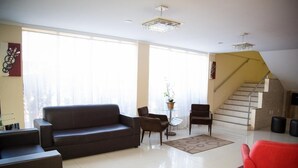 A spacious living room with a dark brown sofa, two armchairs, a small round table, and a staircase leading to an upper level. - Hotel Caribe (Porto Velho)