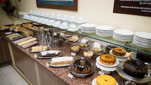 A buffet with various desserts and pastries, including cakes and donuts, displayed on a counter with plates and cups. - Hotel Caribe (Porto Velho)