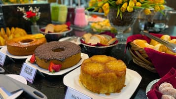 Um buffet com diversos doces, como um donut coberto de chocolate, um bolo invertido de abacaxi e um prato de biscoitos com açúcar de confeiteiro.