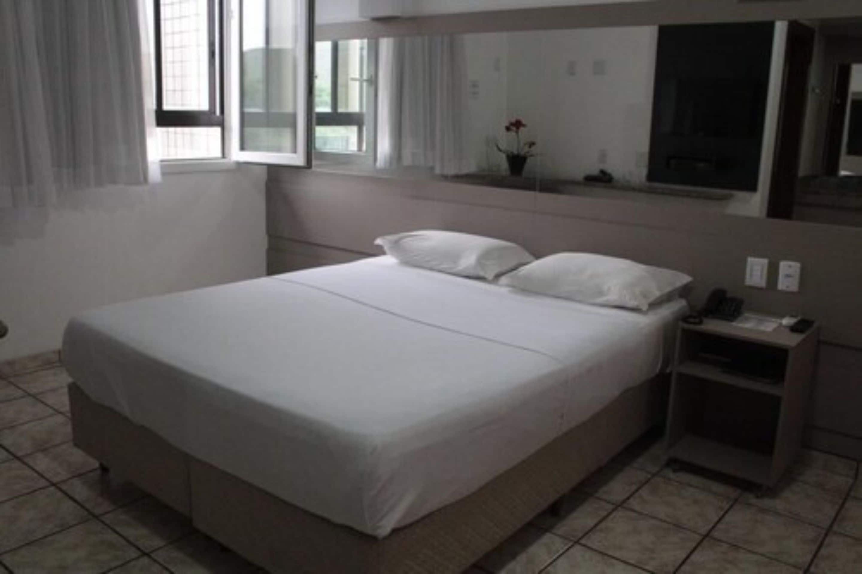 A neatly made bed with white linens in a hotel room.