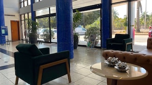 Eine Hotelhalle mit großen Fenstern, blauen Säulen und einer Rezeption mit Theke und Sesseln.