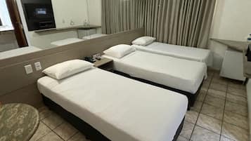 A hotel room with two single beds, a small table, a TV, and a mirror.