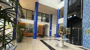Eine großzügige Lobby mit hohen Decken, blauen Säulen, einem großen Sofa, einem Couchtisch und einem Blumentopf.