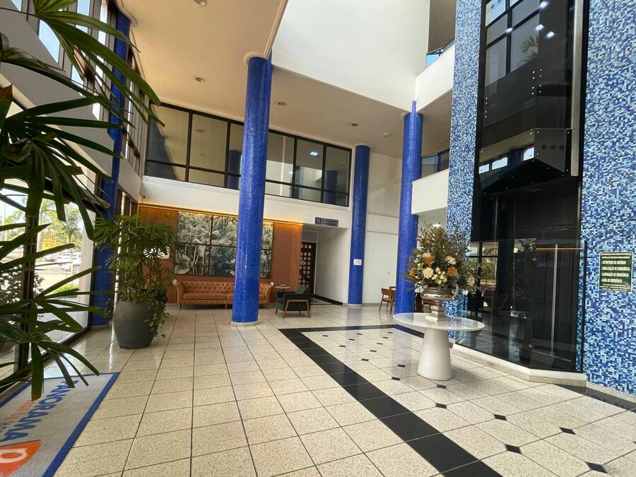 Een ruime lobby met hoge plafonds, blauwe pilaren, een grote bank, een bijzettafeltje en een potplant.