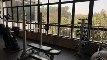 Un gimnasio con equipo de levantamiento de pesas, una banca y amplias ventanas con vistas a zonas verdes.