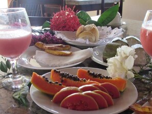 A table with various dishes including sliced papaya, a red drink, and a plate with a flower arrangement.