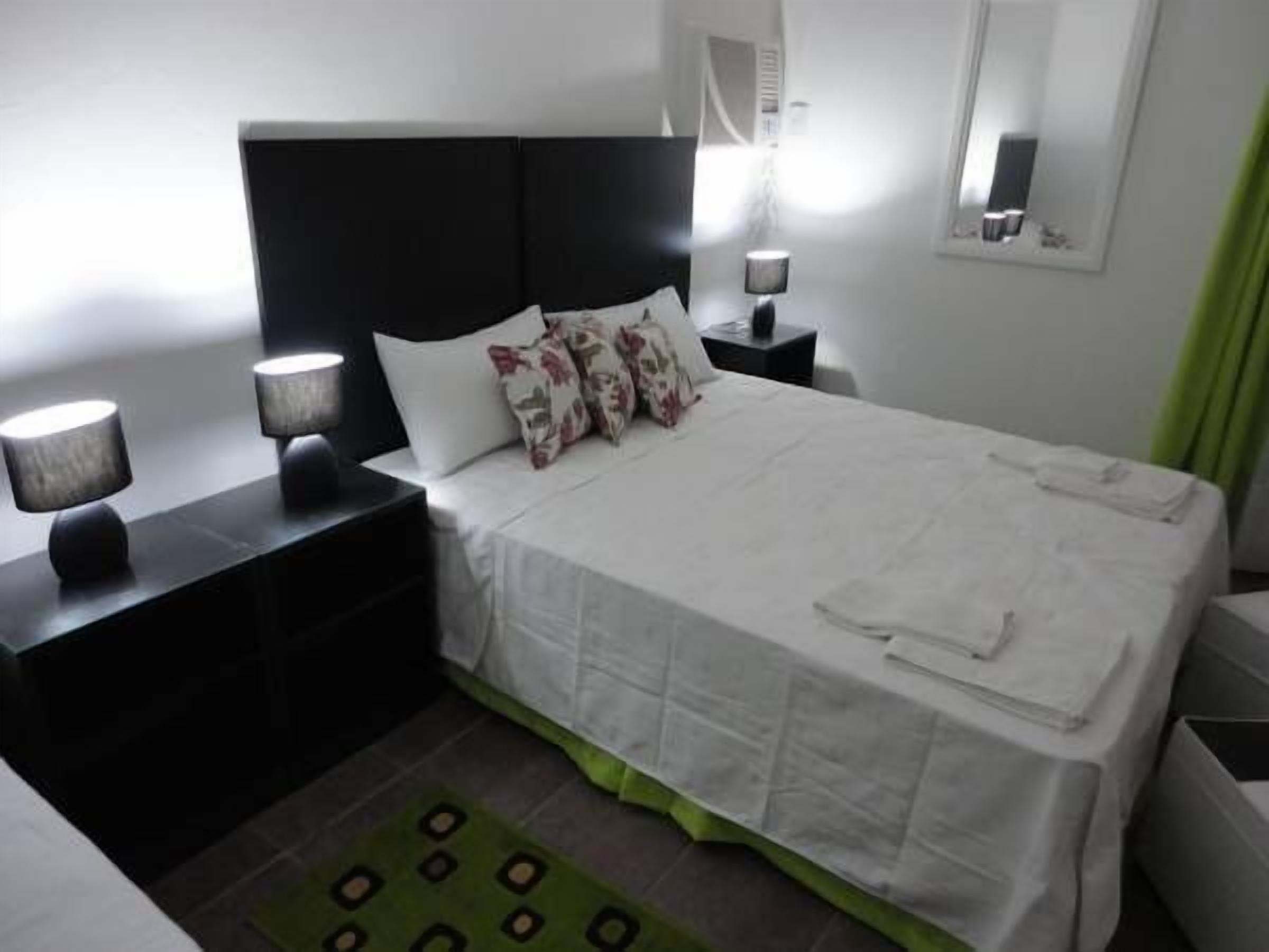 Una habitación de hotel con una cama grande, una mesita de noche con lámpara, un tapete estampado verde y un espejo en la pared.