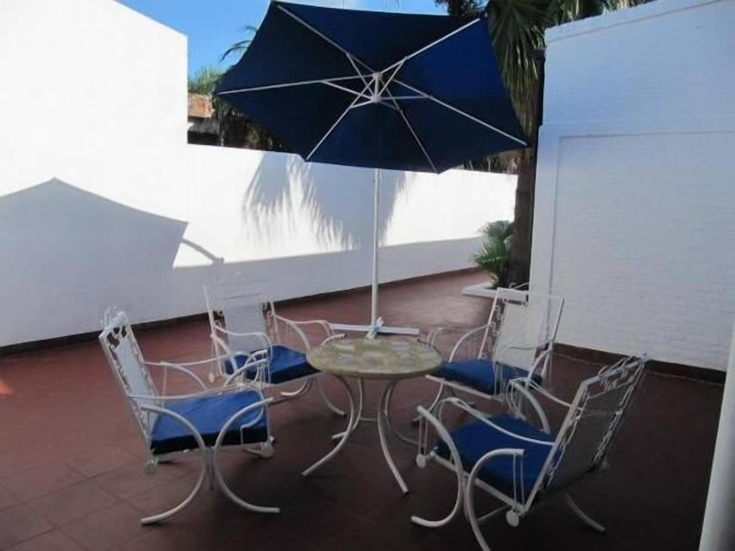 Een terras met een ronde tafel, vier stoelen, een parasol en een witte muur.