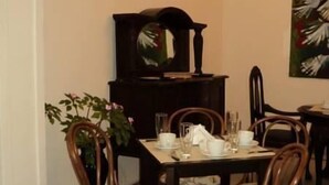 A dining area with a wooden table set for four, surrounded by floral-patterned chairs. A potted plant is on the left, and a painting is on the wall to the right. - Ñanderoga (Corrientes)