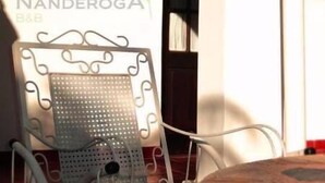 A chair with a perforated backrest and a blue cushion, positioned in front of a wall with a sign reading "NANDEROGA B&B". - Ñanderoga (Corrientes)