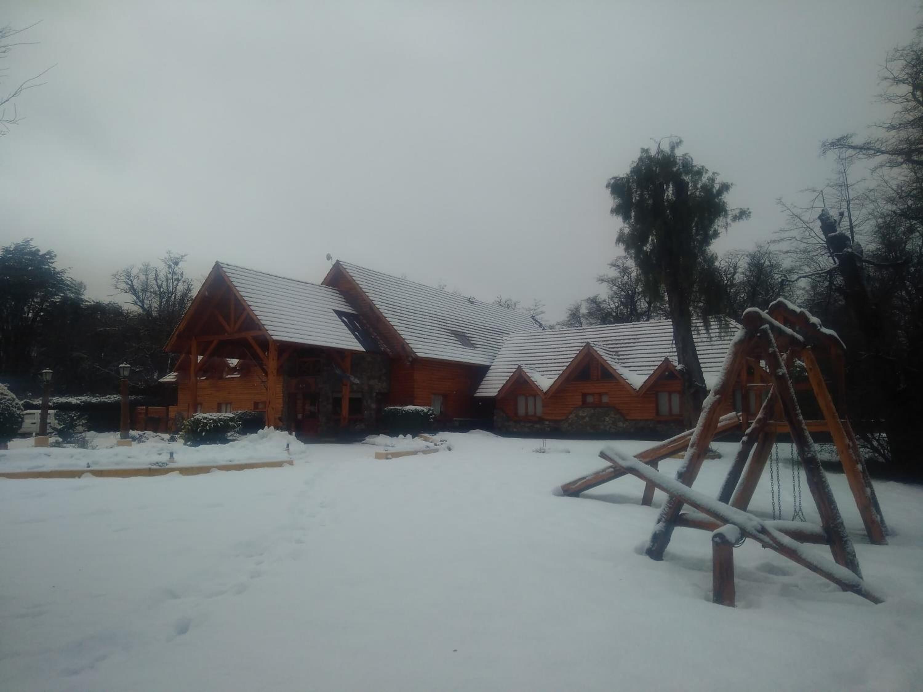 Une cabane en rondins avec un toit enneigé et un portique dans la cour.
