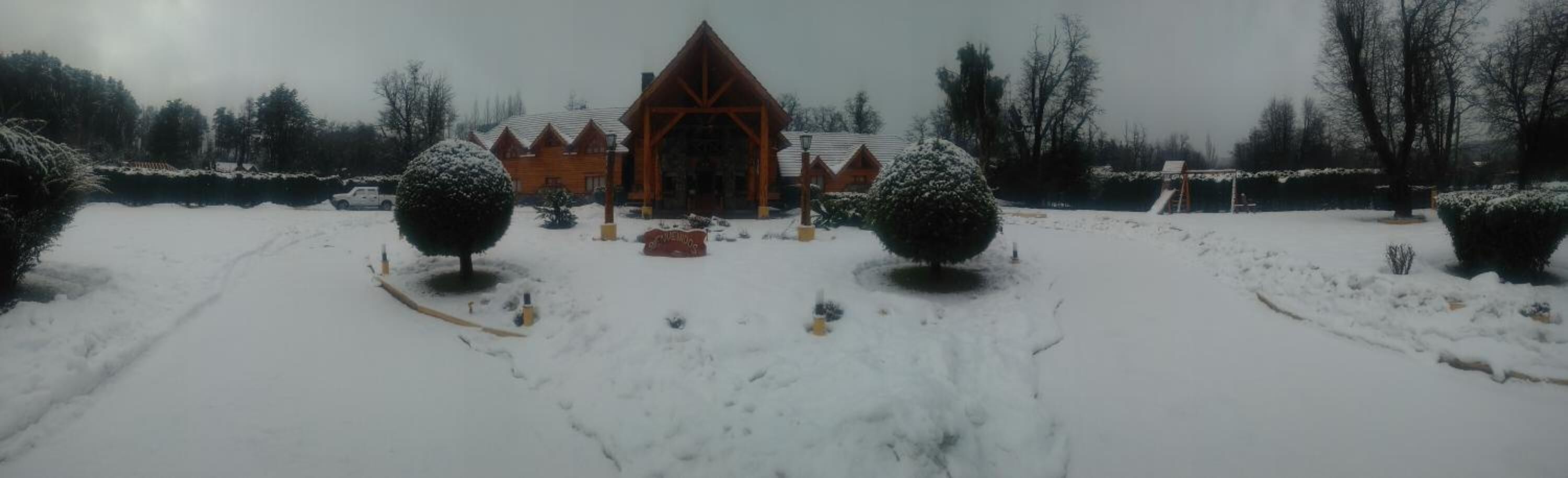 A snow-covered lodge with a central building and two symmetrical trees.