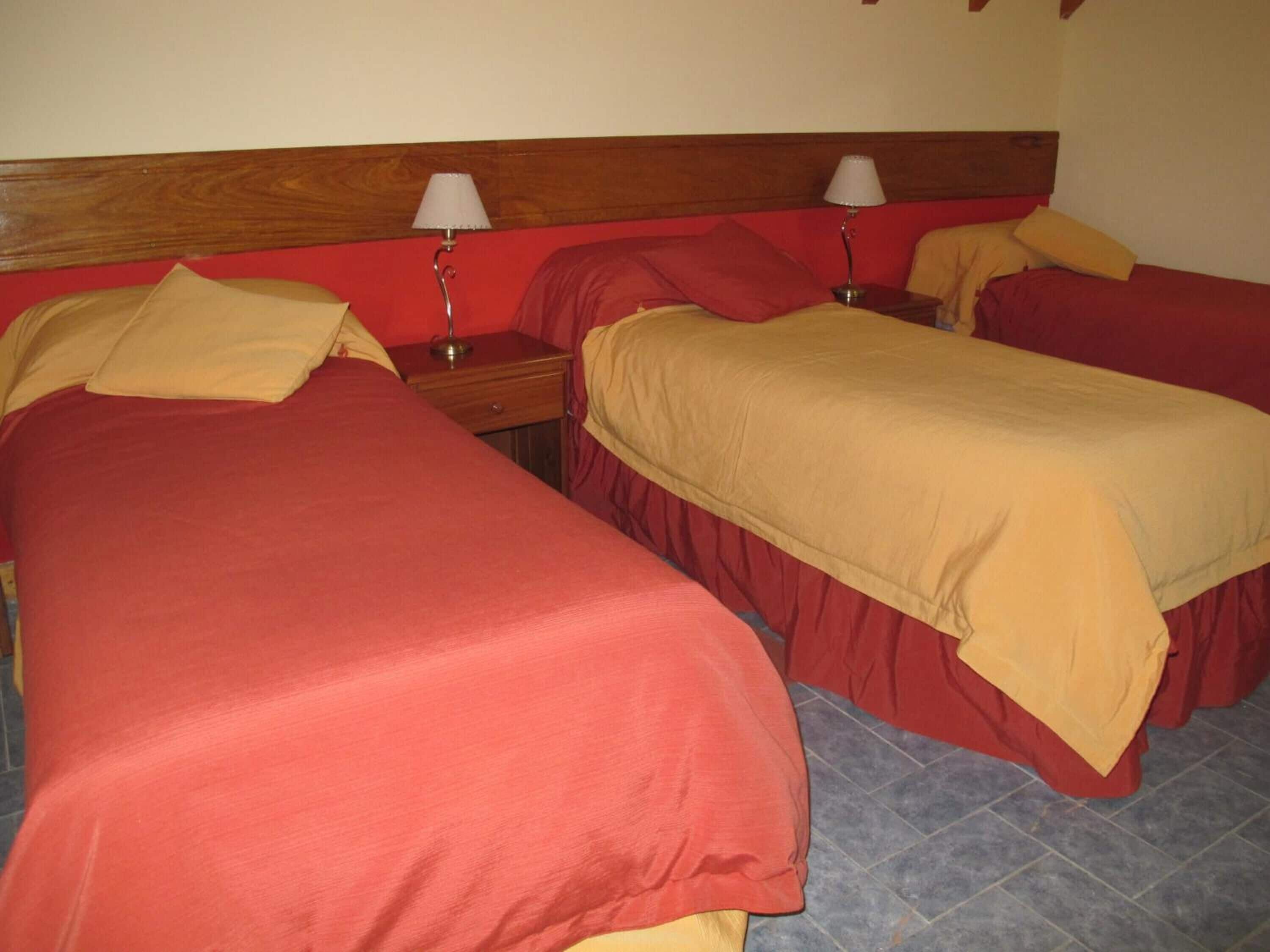 Une chambre d’hôtel avec deux lits, chacun agrémenté de draps rouges et beiges, et deux lampes de chevet.