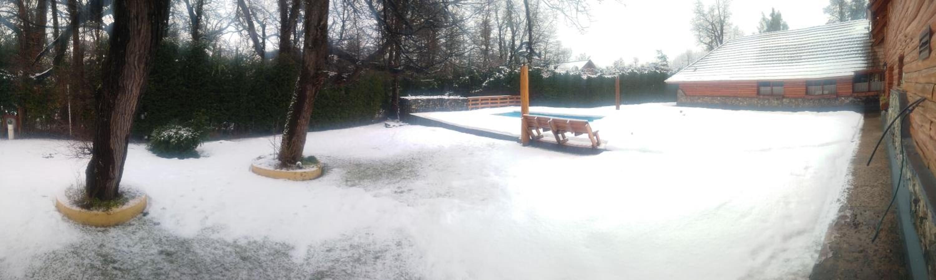 Un patio nevado con una terraza de madera y una piscina.