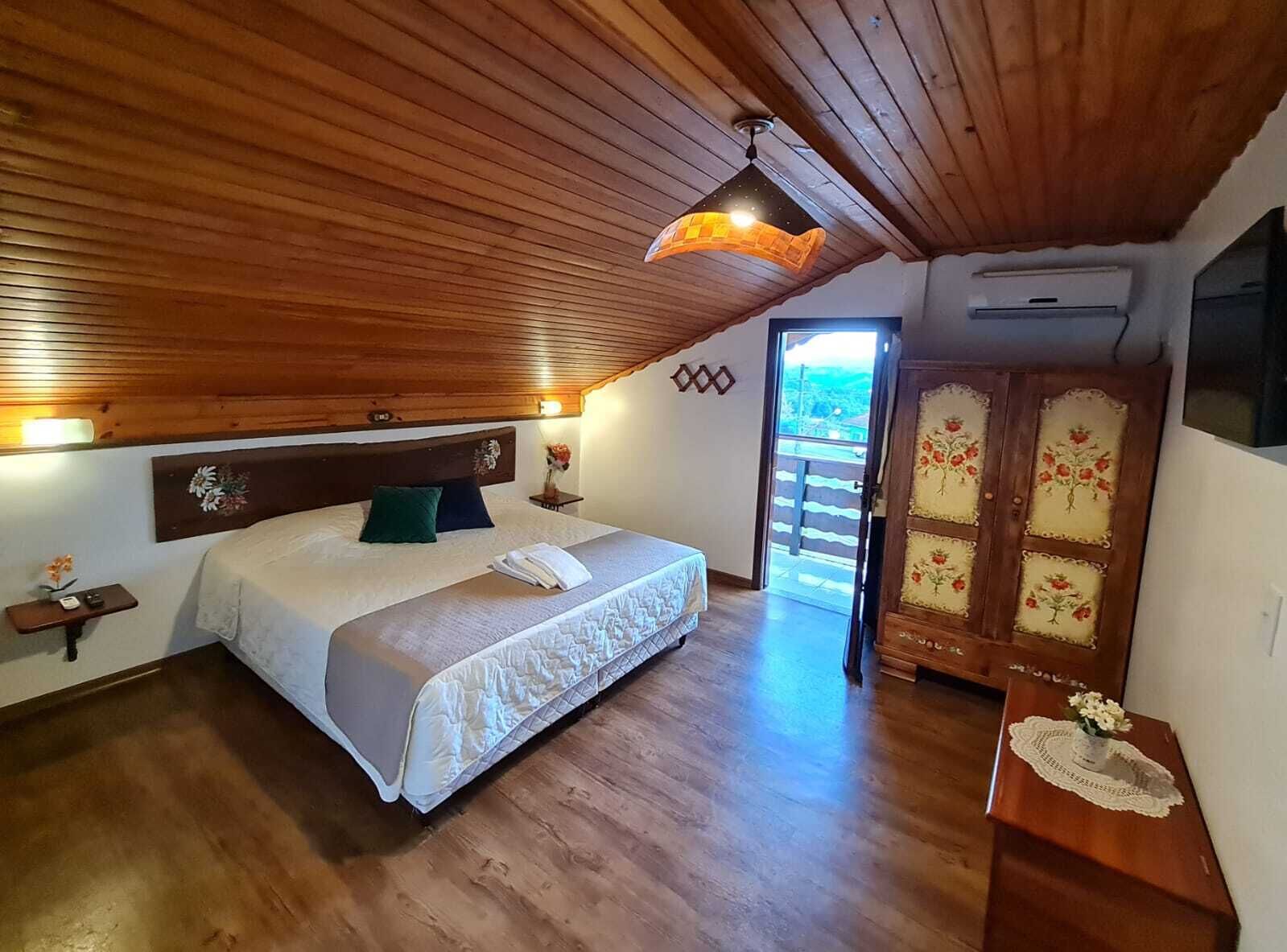A bedroom with a wooden ceiling, a bed with a white duvet, a nightstand with a vase, and a door with floral designs.