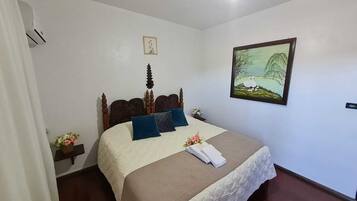Una cama bien hecha con cabecera de madera, un cuadro de paisaje enmarcado en la pared y una mesita de noche con un florero.