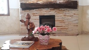 Una habitación con pared de piedra, chimenea, mesa de centro de madera con un jarrón de flores y una escultura.