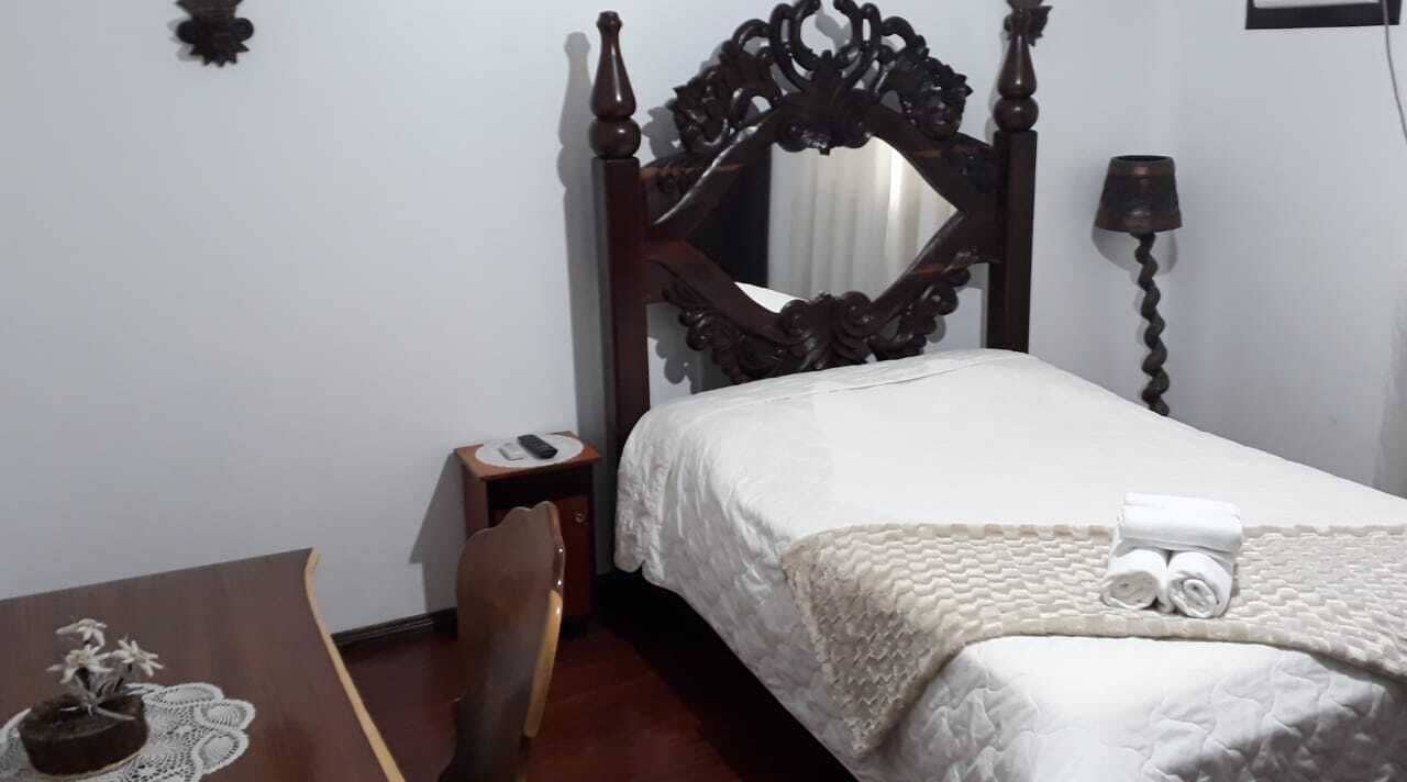 A neatly made bed with a wooden headboard, a bedside table with a lamp, and a chair.