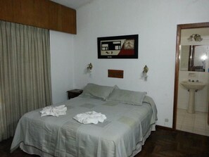 Ein Hotelzimmer mit Bett, Nachttisch, Wandbild und einem durchgegangenen Tür sichtbaren Badezimmer.