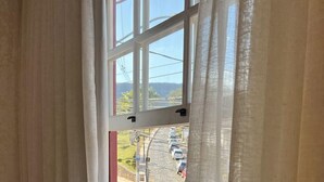 Una ventana con cortinas blancas, vista a una carretera con coches, y un cielo despejado.