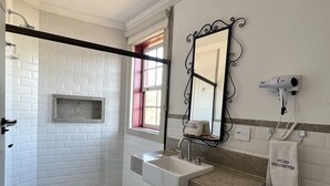 Un baño con ducha, lavabo, inodoro, un toallero y una ventana con cortinas.