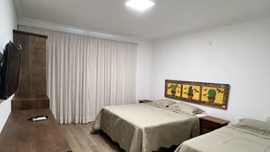 Habitación de hotel con dos camas, un escritorio de madera, un televisor de pantalla plana en la pared y una ventana con cortinas.