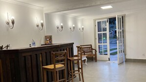 Zona de recepción con mostrador de madera, taburetes de bar, luminarias fijadas a la pared y puerta de cristal que da al exterior.