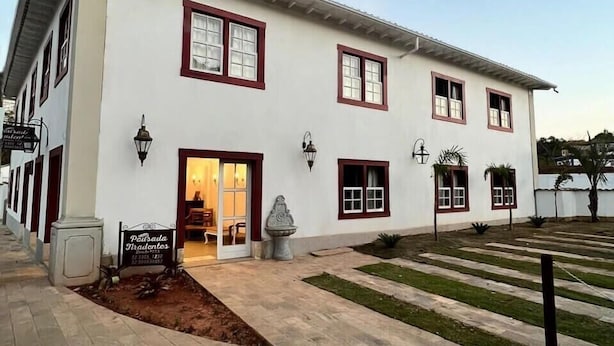 Un edificio de dos pisos con fachada blanca y marcos de ventana rojos, un área de entrada pavimentada y un letrero.