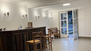 Zona de recepción con mostrador de madera, taburetes de bar, luminarias fijadas a la pared y puerta de cristal que da al exterior.