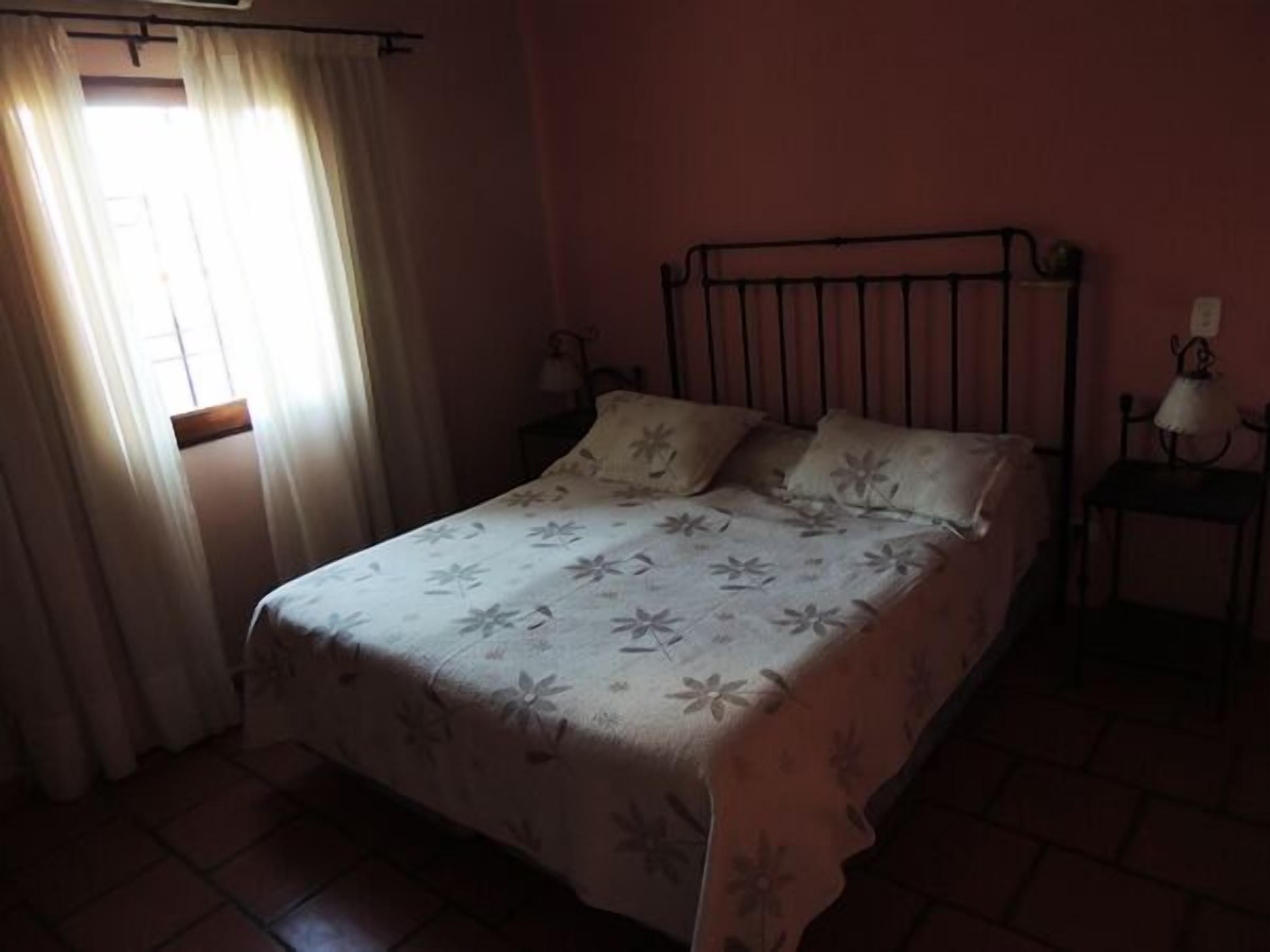 Una cama individual con una colcha estampada, una mesita de noche con una lámpara y una ventana con cortinas.