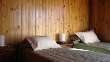 Una habitación con paredes de madera, dos camas con almohadas, una mesita de noche y una lámpara.