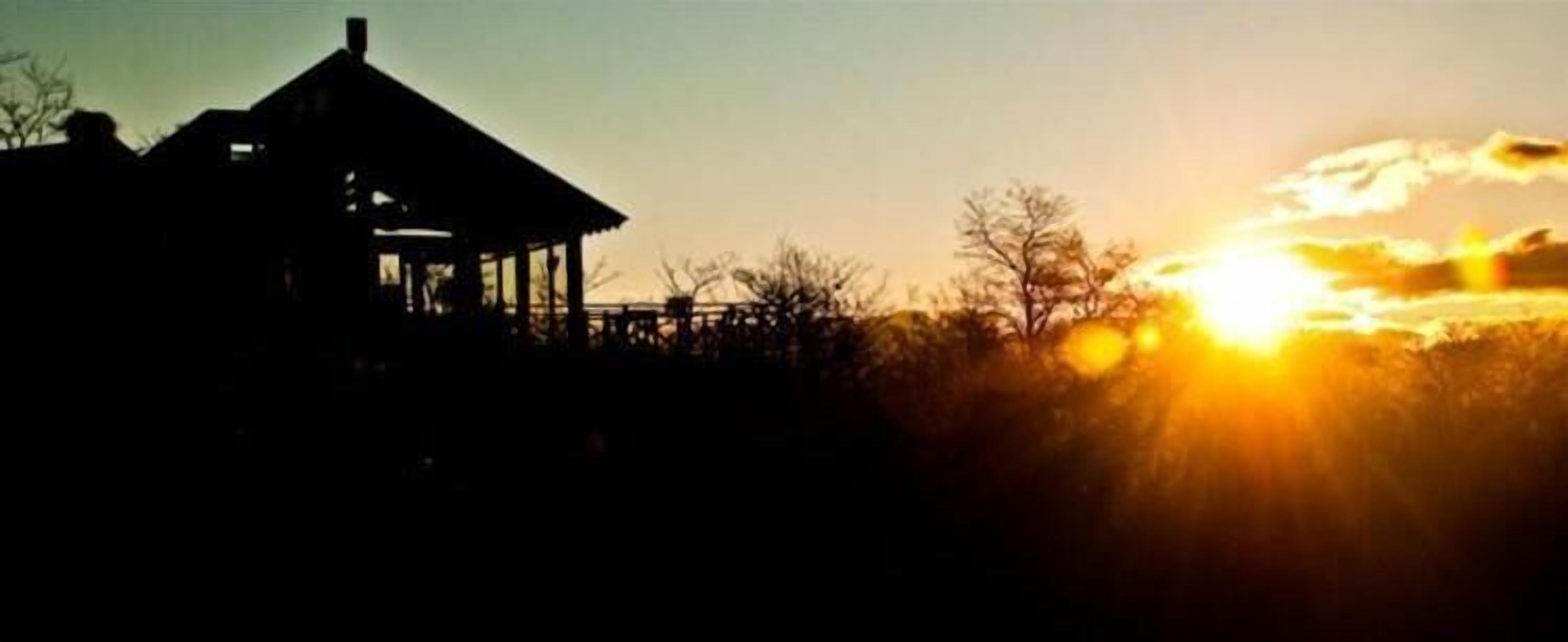 La silhouette d’un bâtiment doté d’un toit et d’une zone abritée, peut-être un pavillon ou un kiosque, se détache sur le ciel d’un coucher de soleil.