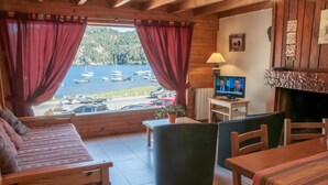Ein gemütliches Blockhaus mit Holzeinrichtung, einer Couch, einem Tisch und einem Fernseher, der eine Nachrichtensendung zeigt.