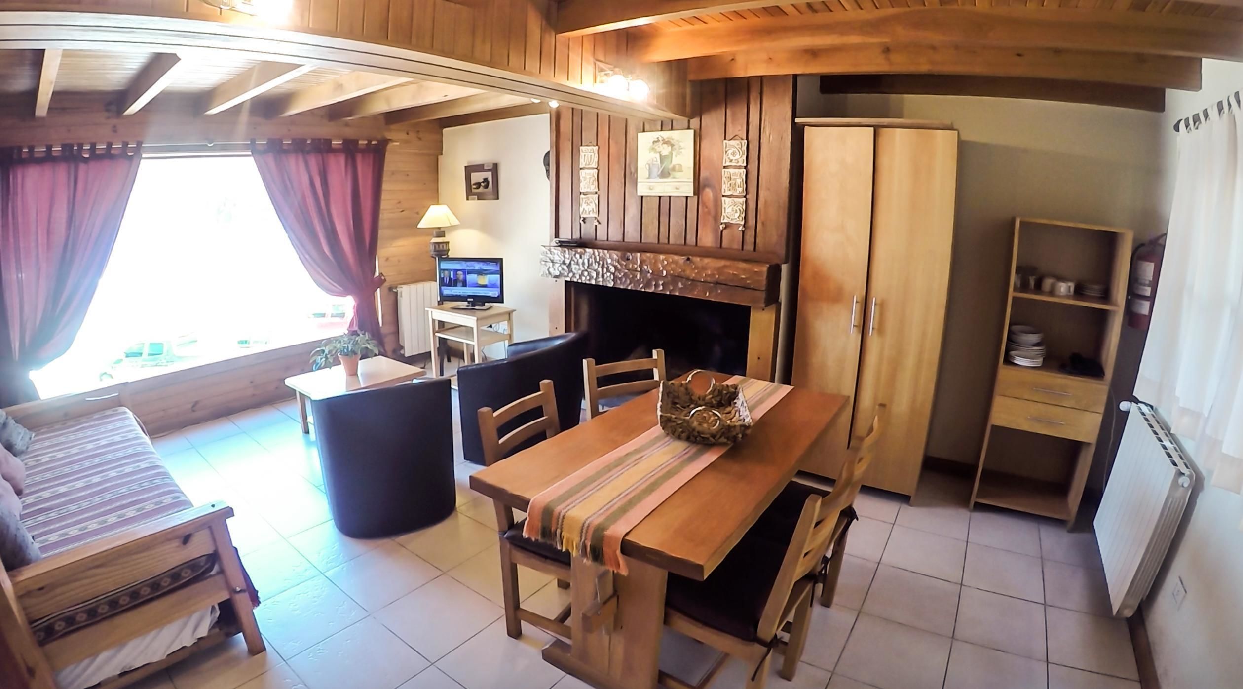 A cozy wooden room with a dining table, chairs, a television, and a fireplace.