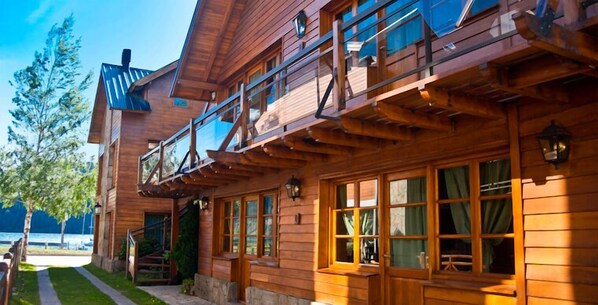 A wooden cabin with a balcony, large windows, and a stone pathway leading to the entrance.