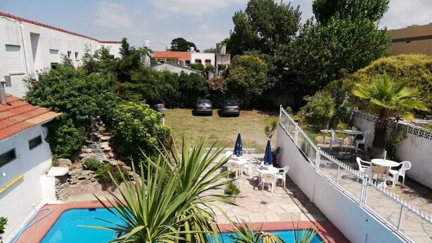 Una piscina con cerco blanco, rodeada de palmeras y un área de patio con sillas y mesas blancas.