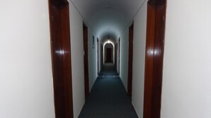 Un largo y estrecho pasillo con puertas de madera a cada lado y suelo alfombrado.